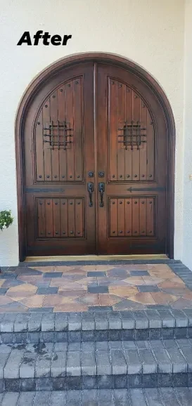 The same arched wood double doors after refinishing, restored to a deep even walnut finish