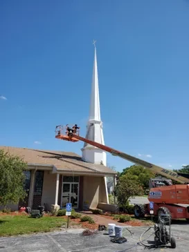 Painters working from a boom lift on a white church steeple against a blue sky