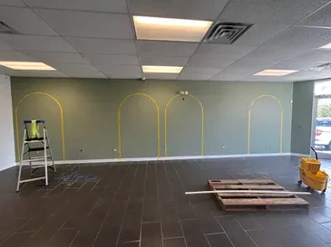 Commercial interior mid-project, with sage green walls and arch shapes masked out in tape before painting