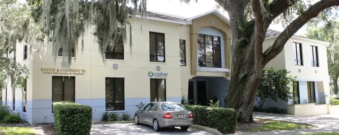 Two-story professional office building painted in cream and white, shaded by live oaks