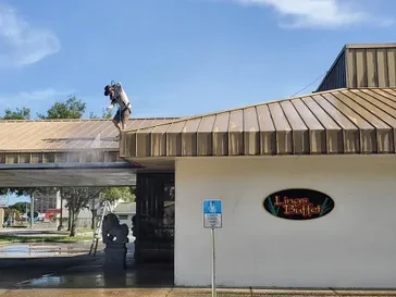 Worker pressure washing a standing-seam metal roof on a commercial building